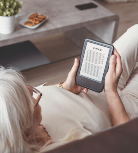 Senior woman sitting by the window reading an E-book