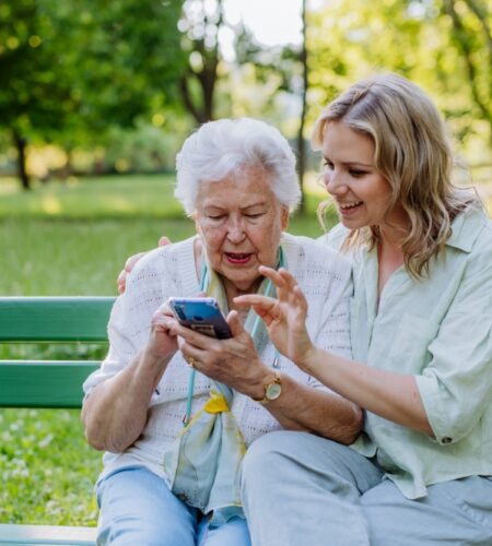 Adult granddaughter helping her grandmother to use cellphone